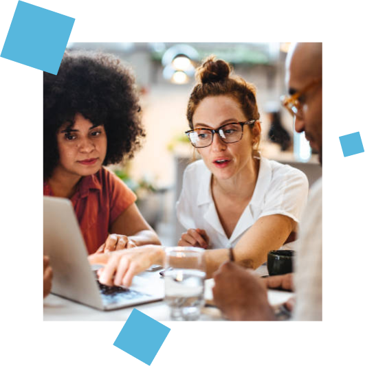 Two women and a man looking at the screen of a laptop computer. Woman is pointing at something on the screen.